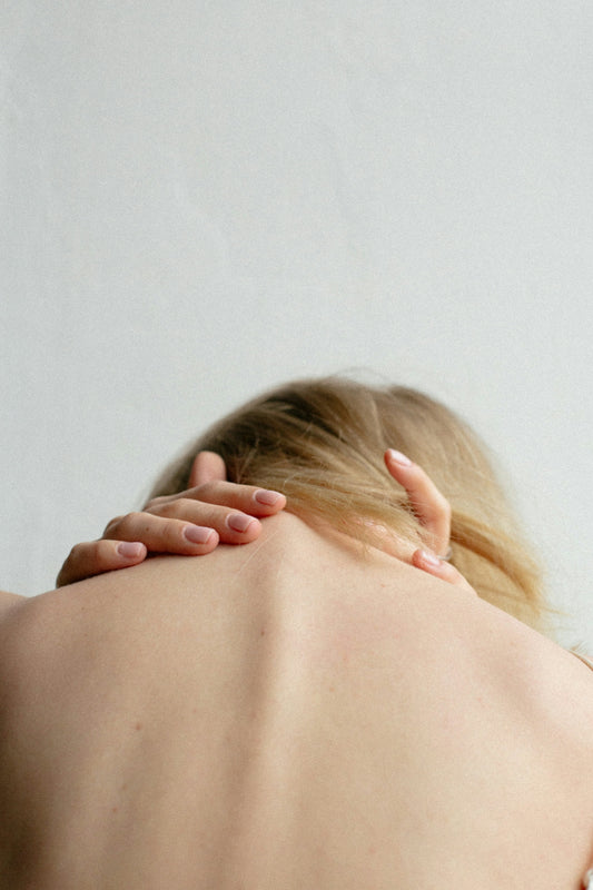 A person with blonde hair touching the back of their neck with both hands